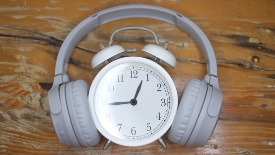 Front View Alarm Clock put on headphones on wooden table. Timeless Music Concept. Concept of time listening to music.