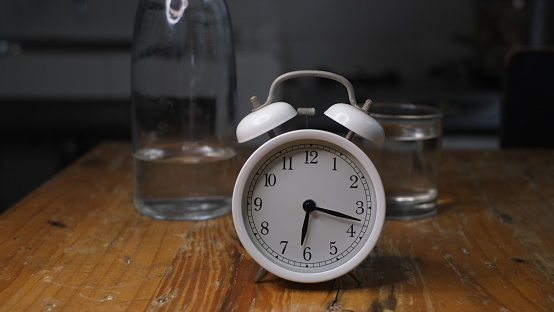 Alarm clock, a glass and a bottle of water on dark background, close up, conceptual photo, reminder to drink water to replace body fluids