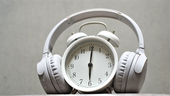 Retro alarm clock with headphone on the plastic table with grey background. Timeless Music Concept. Concept of time listening to music