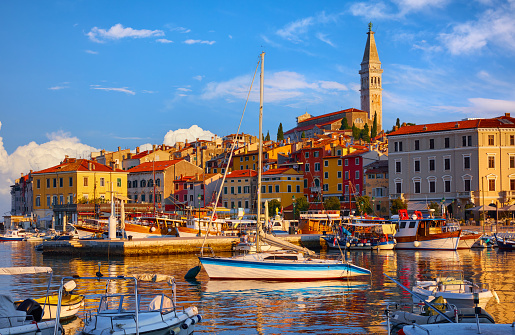 Rovinj, Croatia. Motorboats and boats on water in port of Rovigno. Medieval vintage houses rovinj old town. Yachts landing, tower with clock. Morning sunrise Istria blue sky withclouds