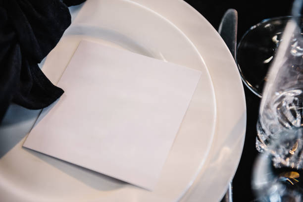 istock Wedding table place with invitation card top view. Blank paper card flat lay. Serving, setting table. Plate decorated linen black napkin, postcard, cutlery, glasses. Set up, dinner table reception. 1692151258
