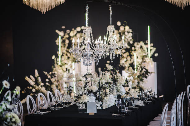istock Luxury wedding reception. Trendy decor large chandelier for a birthday party. Table setting, setup. Banquet decoration composition flowers, candles in hall restaurant. Table covered black tablecloth. 1692151319