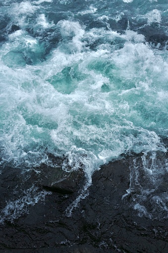 Blue, storming, thunderous water beside a dark rock side. Majestic green blue colored , powerful elevating picture.