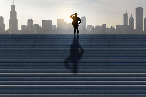 Side view of businessman silhouette looking into the distance on stairs with shadow and city skyline in the background. Success, tomorrow, future and vision concept