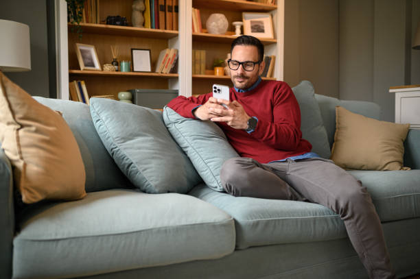 istock Handsome young man browsing social media on smart phone while relaxing on sofa in living room 1692154144
