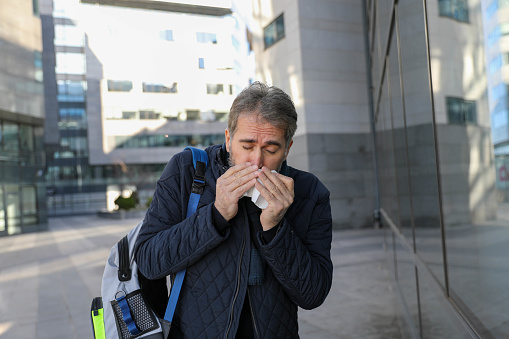 Modern businessman is blowing nose while sitting on the bench in the city.