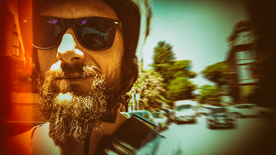 Portrait of a long beard middle eastern ethnicity hipster young man natural smiling with sunglasses behind of motorcycle looking at the camera on outdoor urban scene