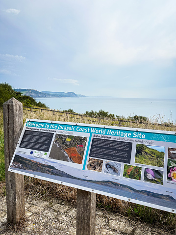 Lyme Regis, Dorset, UK - September 10th, 2023:  A welcome sign with information about the Jurassic coastal erosion and the habitats. View of Golden Cap in the distant.