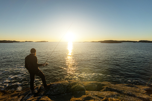 POV man fishing with a rod in the sea by a fjord, in Norway