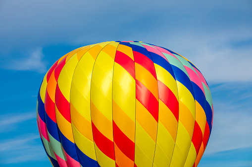 The top of a colorful hot air ballon against a blue sky.