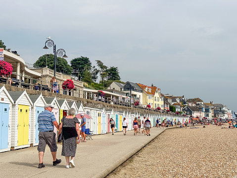 Lyme Regis, Dorset, UK - September 10th, 2023: People strolling along vibrant beach huts on a late Summer day,