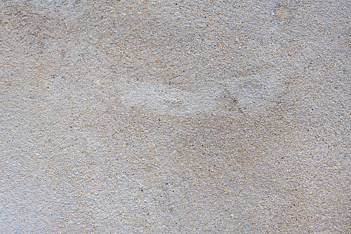 The surface of a raw concrete wall features a grainy, harsh, raw, uneven, and porous texture.