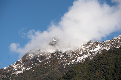Clouds drift across the the face of a snowcapped mountain in New Zealand's Southern Alps. In the bottom left of the image a tourist helicopter can be seen passing over the mountain ridge.