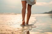 Closeup of woman feet walking on sand beach during a golden hour sunset. Travel and relaxing in summer