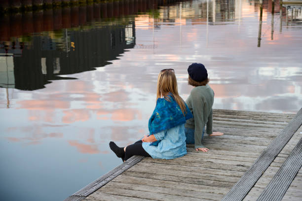 Two adult women having a nice time at the waterfront. Rear view portrait of women in conversation in front of water reflecting sky