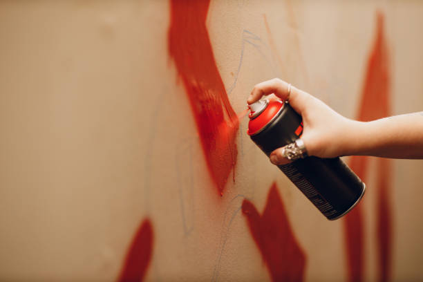 mujer joven con un globo de spray con pintura en la mano en una máscara protectora pintando graffiti de arte callejero en el garaje - graffiti men wall street art fotografías e imágenes de stock