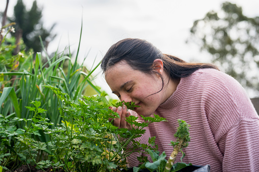 Side view portrait of woman with down syndrome smelling aromatics plants while doing gardening