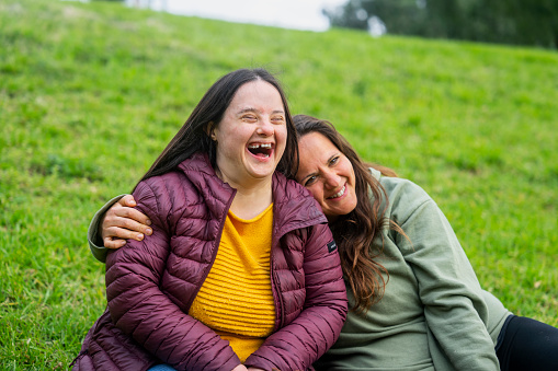 Portrait of woman with down syndrome laughing while sitting in grass with mother during daytime