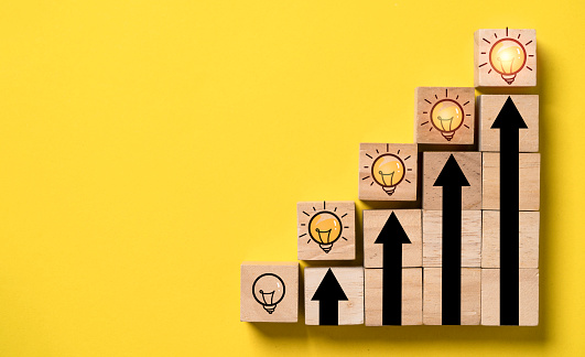 Glowing lightbulb on the top of up arrow and wooden block cube for human development of problem solving solution and creative thinking idea innovation concept.