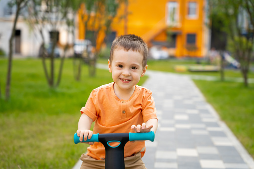 A cute happy toddler boy of two or three years old rides a bicycle or balance bike in a residential complex on a sunny summer day. Active kid playing outside. Close up