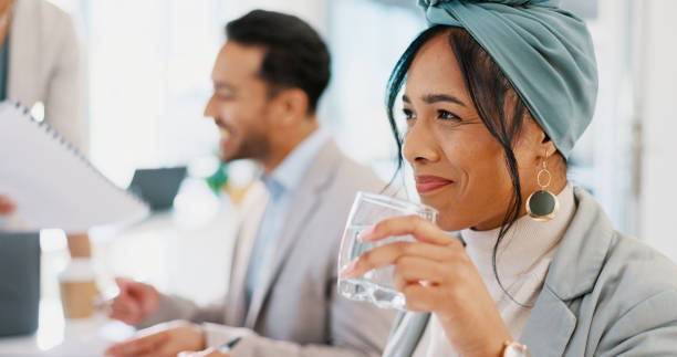 mujer de negocios, bebiendo agua y sonriendo en la cara mientras está en una reunión corporativa para planificar una colaboración con un equipo. emprendedora feliz y pensando en la idea mientras está en el taller o la capacitación - office water business meeting fotografías e imágenes de stock