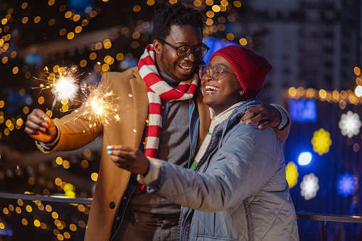 A young woman and a young man holding sparklers in their hands and enjoying the December holidays outdoors