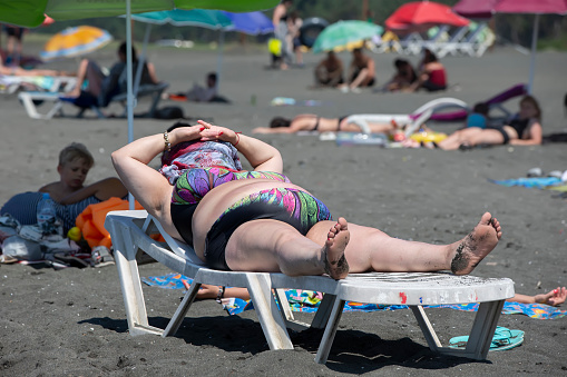 August 6, 2022. Georgia, Ureki village. Beach with black magnetic sand. A plump woman is sunbathing on a sun lounger on the beach.