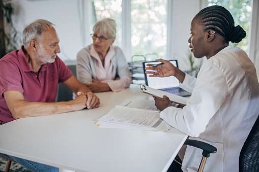 Three people, senior couple sitting in doctor's office with a female doctor.