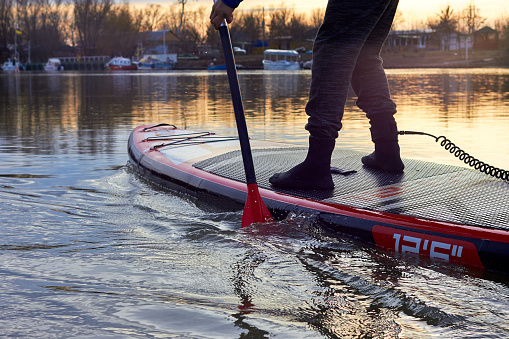 Men's legs on SUP (stand up paddle board) in water of the autumn river at sunset