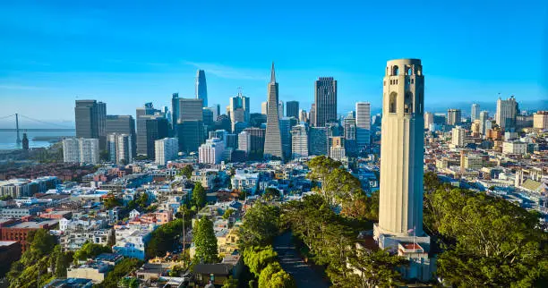 Photo of Aerial Coit Tower in late afternoon with downtown San Francisco skyscrapers and distant bridge