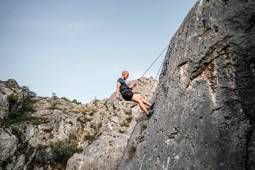 Young man with a rope climbing on the vertical cliff rock wall