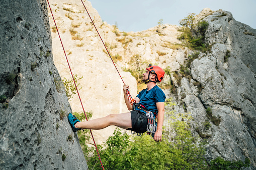 Young man climber in protective helmet with rope climbs on the route