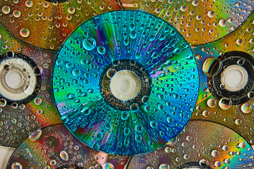 Image of Colorful and vibrant blue CD surface with water drops stacked on top of pile of CDs abstract art