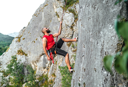 Young Caucasian athletic man climbs a rock with a rope