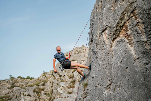 Young man using rope while climbing on vertical cliff rock wall