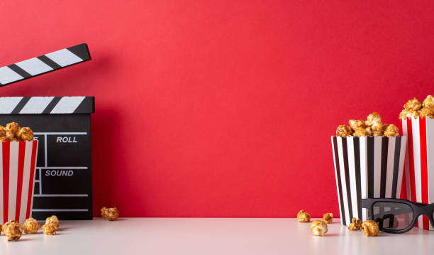 istock Cinematic anticipation: A side view table displays striped boxes filled with cheese and caramel popcorn, 3D glasses, and a clapperboard against a red wall, setting scene for a movie premiere gathering 1692386381