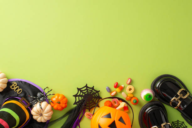 istock Captivating children's Halloween celebration scene. Top view image displaying sweets, kid's costume accessories, and spooky decorations on green isolated background, suitable for ads or text 1692386526