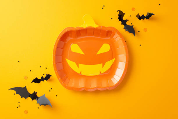 istock Get into the Halloween mood with this creative table setting. Top-down view of themed tableware, such as jack-o'-lantern plate. Eerie decorations like bats and themed confetti on orange background 1692386853