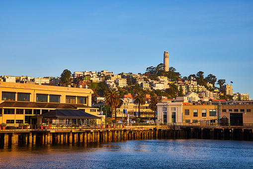 Image of Shoreline at golden hour with docks on San Francisco Bay looking up at Telegraph Hill and Coit Tower