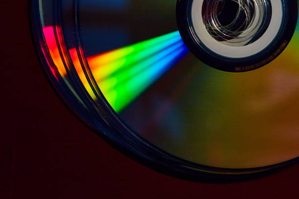 istock Stacked CDs in dark setting with cone of rainbow colored light shaft across silvery surface 1692398490