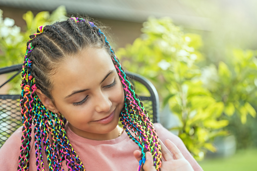 Portrait of  young girl with beautiful colorful braids looking down.  Horizontally.