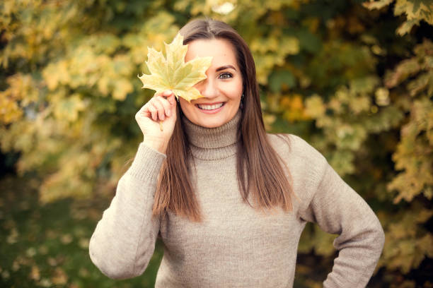 秋の木の背景にカエデの葉を顔に持つ少女の接写 - 金運　顔 ストックフォトと画像