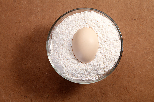 Uncracked egg on top of a bowl of flour.