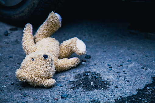 Conceptual image: lost childhood, loneliness, pain and depression. Teddy bear lying down outdoors.
