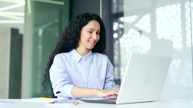 Young positive female employee typing on laptop while sitting at workplace in modern office