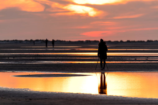 female photographer with tripod at beach against sunset
