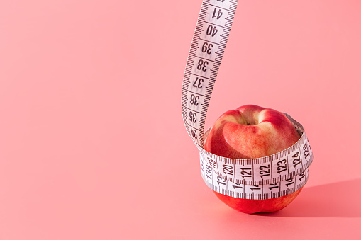 Slimming, body shaping, skin care. Fruit peach is wrapped with measuring tape on pink background
