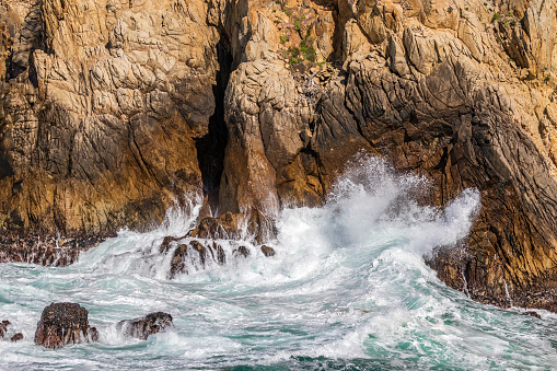 Ocean wave breaking against rocky cliff at Point Lobos Nature Preserve, Monterey, California.
