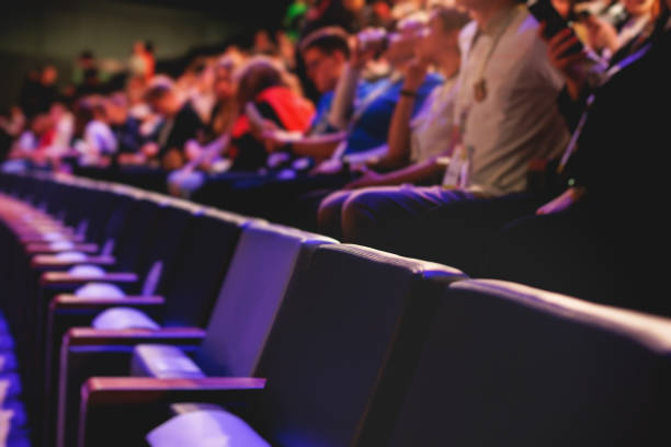 istock Audience at the modern conference hall listens to panel discussion, people on a congress together listen to speaker on stage at convention, business seminar, amphitheater venue for congress 1692553253