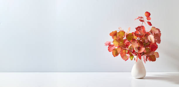 istock Home interior with decor elements. Colorful autumn leaves in a vase on a light background 1692562887